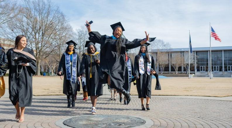 A student jumps in the air while walking across the ODU seal.